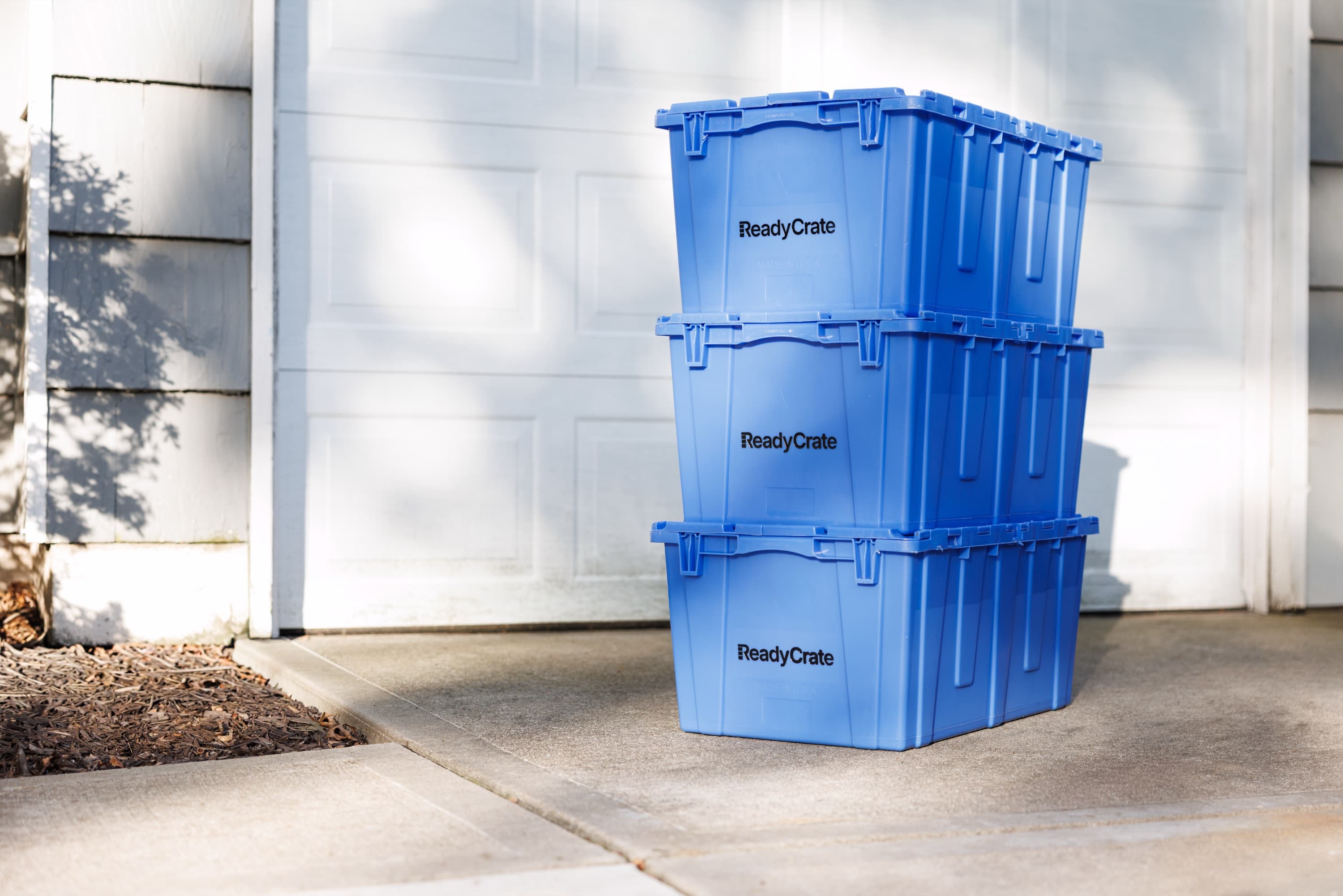 Stack of three blue ReadyCrate totes on a suburban driveway in front of a white garage door